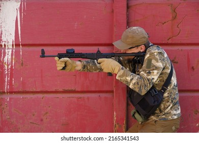 Military Soldier Man In Boot Camp. Man In Tactical Uniform With Gun Or Weapon. Tactical Camp Combat Training. Shooter Man With Gun In Military Uniform Hide Behind Rusty Red Wall. Masculine Hobby