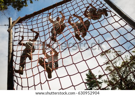 Military soldiers climbing rope during obstacle course in boot camp