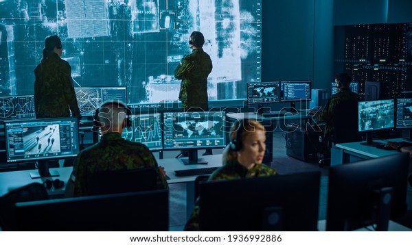 Military Surveillance Team of Officers\
Locked a Target on a Vehicle from a Satellite and Monitor it on a\
Big Display in Office for Cyber Operations for Managing Security\
and Army\
Communications.