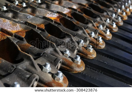 Military tank tracks with screws, bolts, black rubber parts and some rust on metal details, army industry, selective focus 