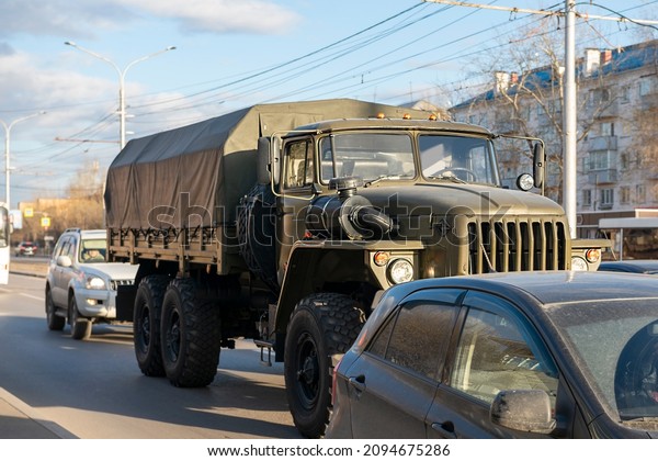 Military\
truck of green color in the traffic flow. Green truck with a\
tarpaulin body. Active car traffic in the\
city.
