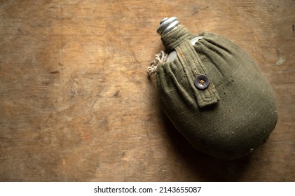 A Military Water Flask On A Wooden Table. An Old Flask In A Case.