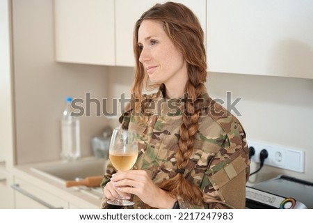 Military woman stands in the kitchen with a filled glass