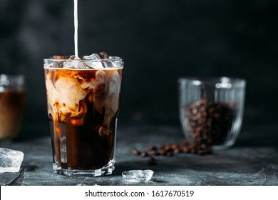 Milk Being Poured Into Iced Coffee on a dark table