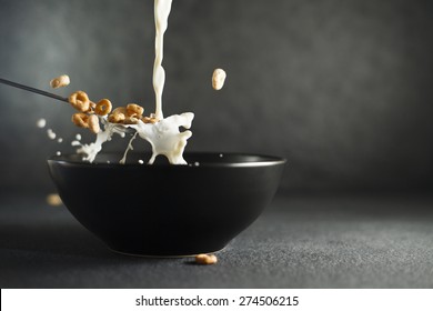 Milk being poured on ring cereals in spoon over dark bowl on dark background