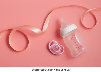 Milk Bottle Baby And Pacifier With Ribbon Around On Pink Background