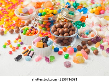 Milk chocolate candies woth shell in jar with various jelly gums candies on white table with liquorice allsorts and strawberry bonbons with different sour sugar gums.