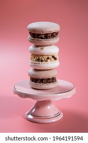 Milk chocolate ganache
refined with coconut puree and a core of coconut. The macaron shells are naturally colored with a touch of cocoa powder. Pyramid of macarons on a pink cake bowl. Pink background