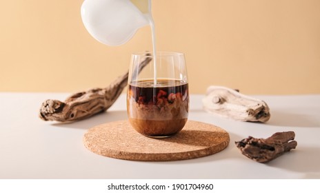 Milk cream pours into a transparent glass of black coffee on a minimalistic beige natural wooden background. Coffee drink cocktail with milk. - Shutterstock ID 1901704960