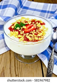 Milk dessert with strawberries, corn flakes and yogurt in a glass bowl, a spoon, a napkin on a wooden boards background