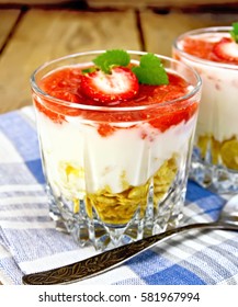 Milk dessert with strawberries, corn flakes and yogurt in a glass, a spoon on blue napkin on a wooden boards background
