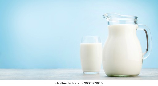 Milk in glass and jug in front of blue background with copy space - Shutterstock ID 2003303945