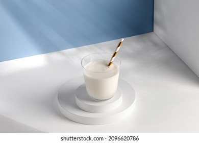 Milk in glass with a straw on white podiums. Natural milk on pedestal in sunlight. Shadow on blue wall. - Powered by Shutterstock