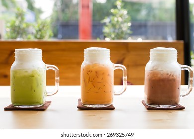 Milk Green Tea, Milk Thai Tea, And Chocolate Drink In Glass Mugs On Wood Table