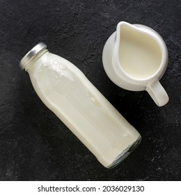 Milk Jug And Bottle Of Milk On A Black Background, Top View.