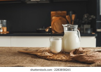 Milk in a jug and a glass, a wooden spoon with oatmeal and ears of wheat on the table. - Powered by Shutterstock