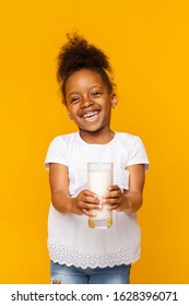 Milk for kids. Smiling black little girl holding glass of milk over yellow studio background