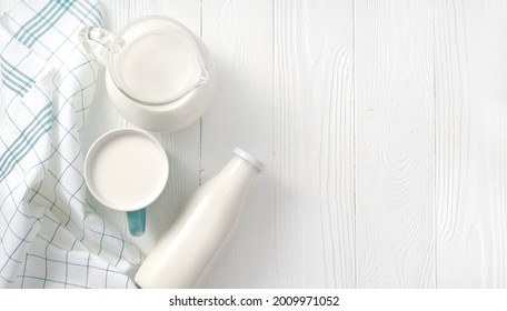 Milk in mug and jug of milk and napkin on white wooden table. Top view flat lay. Bottle of milk on white background with copy space.