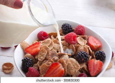 Milk Pour. Milk pouring into bowl of cereals with fresh berries healthy breakfast - berries, fruit and muesli on white wooden table, close-up top view horizontal. Macro shot selective focus