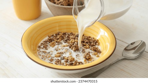 Milk is poured into a plate with granola or muesli. Healthy food. Preparing breakfast. Close-up. - Powered by Shutterstock