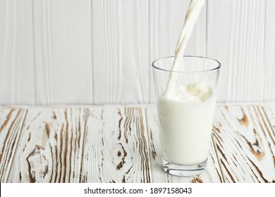 Milk Pouring Into Glass On White Wooden Table