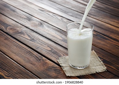 Milk Pouring Into Glass On Wooden Table