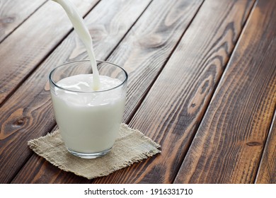 Milk Pouring Into Glass On Wooden Table