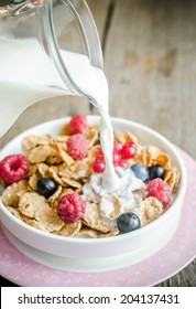 Milk pouring into plate with granola and fresh berries