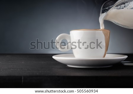 Milk pouring process into cup of coffee. Cup of coffee on dark wooden background.With copyspace for text.