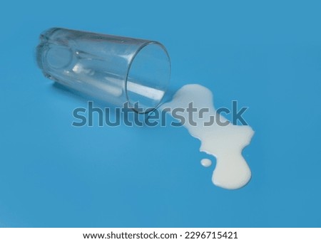 Milk spilled from glass on a blue background.