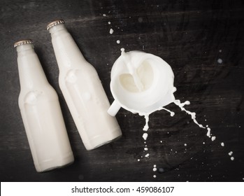 Milk Splash And Bottle Milk On Dark Wooden Table,Top View 