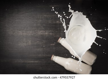 Milk Splash And Bottle Milk On Dark Wooden Table,Top View 