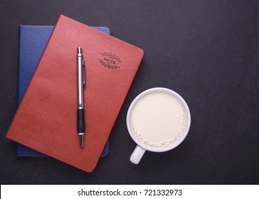 Milk In White Glass And Note Book On Black Stone Table Background. Top View And Studio Shot