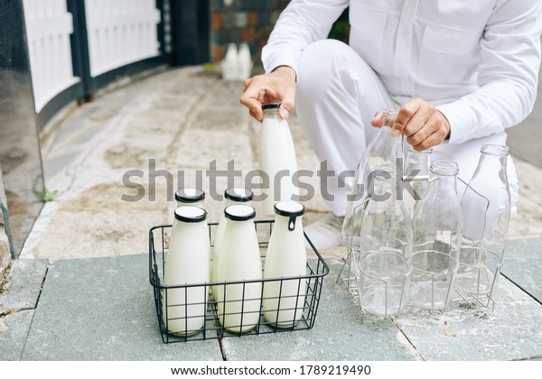 Milkman putting glass milk bottles in wire crane\
and taking back empty\
bottles