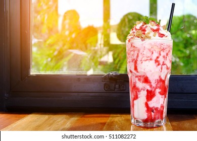  Milkshake with strawberry syrup in glass near the window edge on wood table.