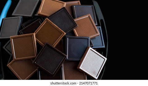 Milchschokolade mit bitterem quadratischem Hintergrund Madlen auf schwarzem Teller mit Kopienraum.Das Zuckerfest oder jede Festivalfeier.Draufsicht
