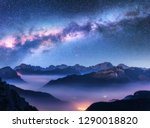 Milky Way above mountains in fog at night in autumn. Landscape with alpine mountain valley, low clouds, purple starry sky with milky way, city illumination. Aerial. Passo Giau, Dolomites, Italy. Space