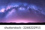 Milky Way arch. Fantastic night landscape with bright arched milky way, purple sky with stars, pink light and hills. Beautiful scene with universe. Space background with starry sky. Galaxy and nature