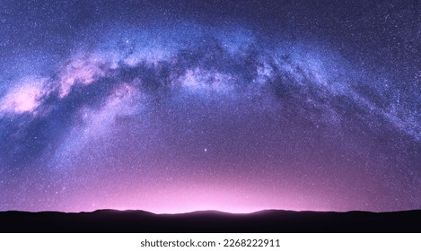 Milky Way arch. Fantastic night landscape with bright arched milky way, purple sky with stars, pink light and hills. Beautiful scene with universe. Space background with starry sky. Galaxy and nature