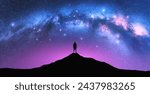 Milky Way arch and man on the mountain peak at starry night. Silhouette of alone guy, pink sky with bright stars in summer. Galaxy. Space background. Landscape with arched milky way. Travel and nature