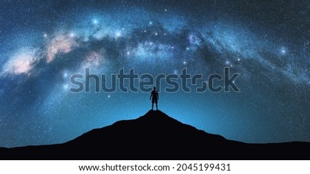 Milky Way arch and man on the mountain peak at starry night. Silhouette of alone guy, blue sky with bright stars in summer. Galaxy. Space background. Landscape with arched milky way. Travel and nature