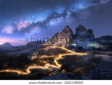 Milky Way, car light trails on mountain road, high rocks at starry night in summer. Tre cime, Dolomites, Italy. Colorful landscape with blurred light trails, hills, mountain peaks, sky with stars