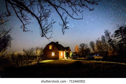 The Milky Way In Night Sky With Stars Over Wooden Country House At Night. Latvia