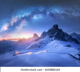 Milky Way over snowy mountains and blurred car headlights on the winding road at night in winter. Beautiful landscape with starry sky, snow covered rocks, house, roadway at sunset. Space and galaxy - Powered by Shutterstock