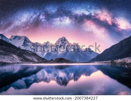 Milky Way over snowy mountains and lake at night. Landscape with snow covered high rocks, purple starry sky, reflection in water in Nepal. Sky with stars. Bright milky way in Himalayas. Space. Nature 