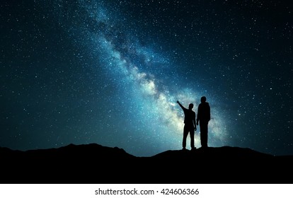 Milky Way with silhouette of a family. Father and a son who pointing finger in night starry sky on the mountain. Night landscape. Beautiful Universe. Space. Travel background with sky full of stars - Powered by Shutterstock