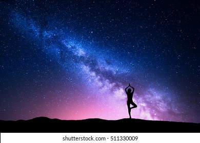 Milky Way With Silhouette Of A Standing Woman Practicing Yoga On The Mountain. Beautiful Landscape With Meditating Girl Against Night Starry Sky With Milky Way. Amazing Galaxy. Universe. Travel 