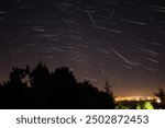 Milky Way stars with meteor shower trails and countryside silhouettes.