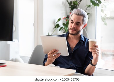 Millenial Business Man Looking At Tablet While Drinking Takeaway Coffee At Home Office - Business Concept