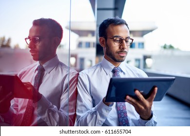 Millenial businessman leaning confidently on a dark glass wall with cityscape background